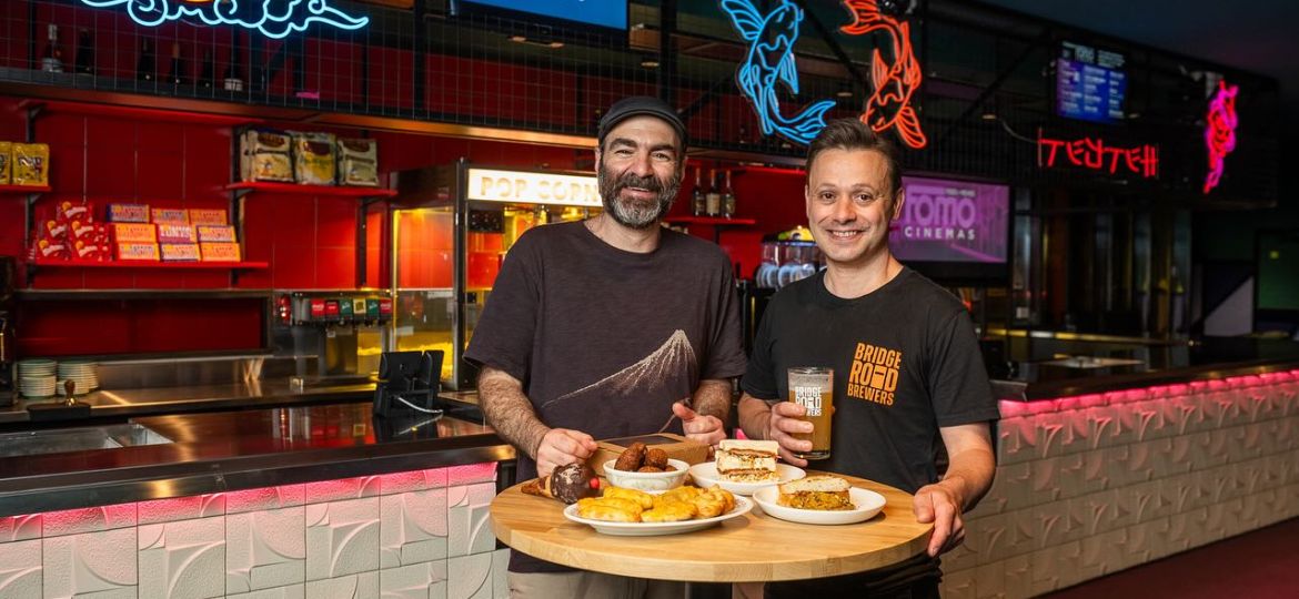two men standing inside at fomo cinemas enjoying food